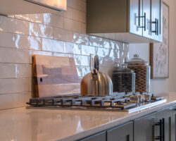 Photo Square frame Kitchen work area with cabinets cooktop countertop and tile backsplash. Dining room in front of a large window can be seen in the background.