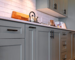 Photo Square Kitchen cabinets with white countertop black handles and tile backsplash. Cooking appliances and wooden floor can also be seen inside this room.